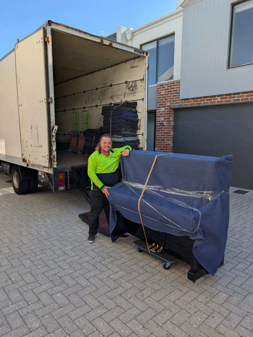 Index Logistics removalist moving a carefully wrapped upright piano beside a removal truck